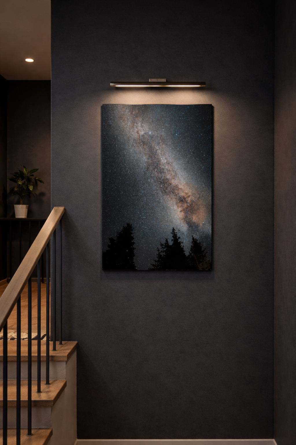 Milky Way metal print displayed on a dark stair landing wall under a picture light, with modern wood-and-black railing nearby